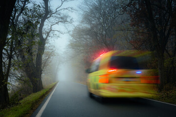 Emergency ambulance speeding on road in heavy fog on gloomy autumn day. Motion blur conveying...