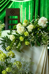 Elegant floral wedding decor with white roses and green foliage against a draped green backdrop