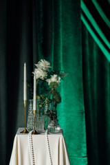 Elegant floral arrangement on pedestal with candles and green velvet curtains