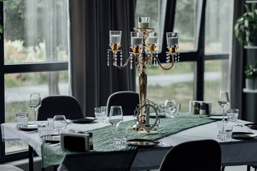 Elegant candlelit dining table with green decor and glassware near large windows