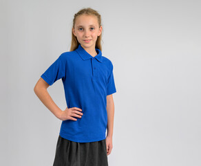Smiling schoolgirl in blue polo shirt and grey skirt posing with hand on hip. Smart, comfortable school uniform made from soft cotton knit texture, ideal for warm weather and everyday wear