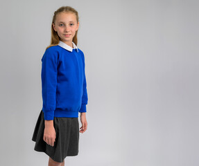 Confident schoolgirl wearing blue pullover and grey skirt, posing against a neutral background. Classic children’s school uniform showcasing cozy knit texture and timeless academic fashion