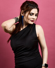 Elegant and confident woman posing gracefully in a black dress on a pink background. Represents modern beauty, fashion, and sophistication.