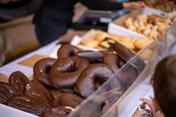 Child choosing fresh chocolate doughnuts at market bakery