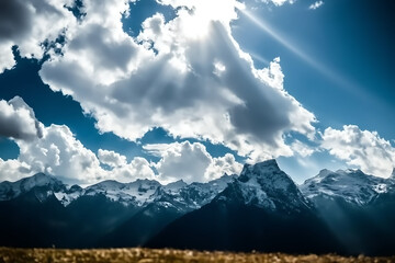 Dramatic sunbeams pierce through fluffy white clouds illuminating a majestic snow capped mountain range under a vibrant blue sky with a golden foreground