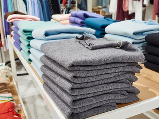 Multicolored T-shirts are stacked on the shelves of a clothing store for sale