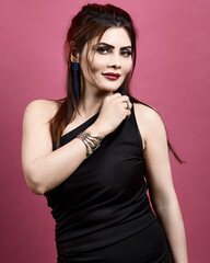 Graceful and confident woman wearing a one-shoulder black dress, posing elegantly in a professional studio with a pink backdrop. Represents empowerment, style, and timeless beauty.