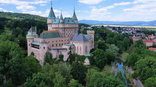 Aerial Bojnice Castle stands majestically amidst a vibrant sea of green, with its picturesque turrets and historic architecture framed by a perfect day. A serene oasis in the heart of Slovakia.
