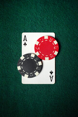 Two poker chips, one red and one black, sit on top of an Ace of clubs card on a green felt table, creating an exciting casino atmosphere in the evening