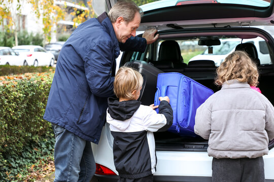 Father and his two children, a son and daughter, loading suitcases into the car trunk as they prepare for an exciting road trip together.
