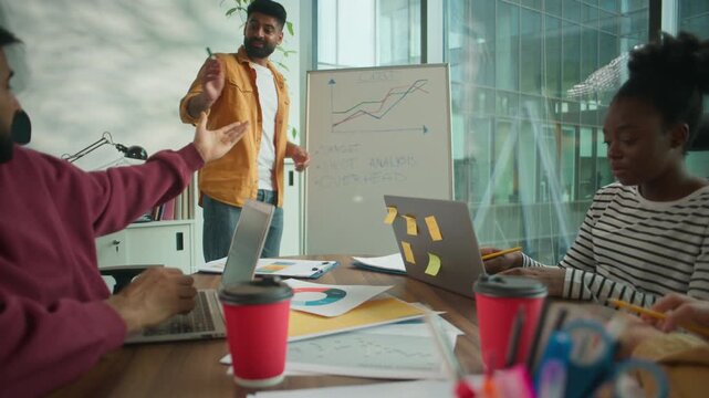 Indian speaker man presenting growth report on whiteboard in office to multiracial business team of four diversity colleagues pointing at marketing charts informal group watching presentation data - Powered by Adobe