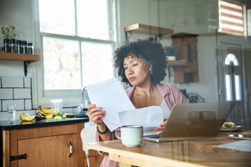 Mature woman reviewing household bills at kitchen table, concerned