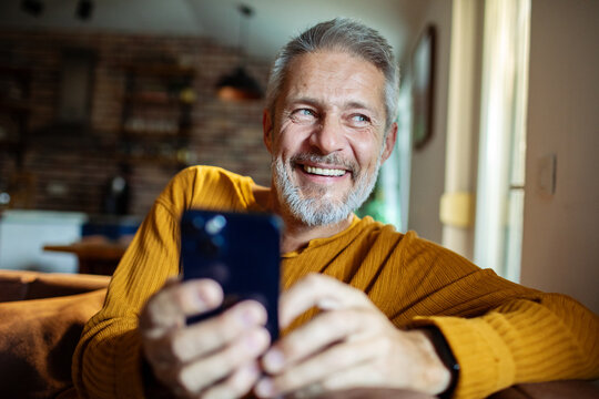 Mature man happy and smiling while using smartphone at home - Powered by Adobe