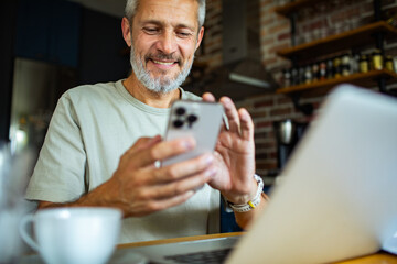 Mature man smiling and using smartphone in home kitchen
