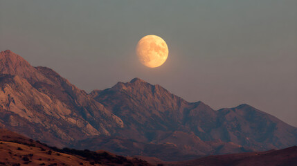 Pale yellow full moon rising behind shadowed mountain range