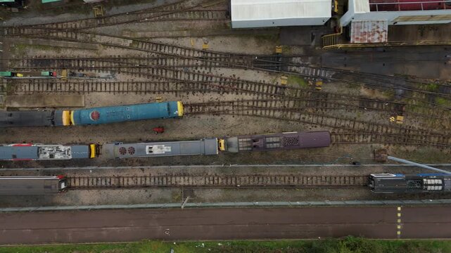Aerial view of parallel train tracks with multiple trains, a building, and other structures, all contrasting in color and texture, Loughborough, United Kingdom.