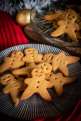 A cozy holiday scene featuring homemade gingerbread man cookies arranged on a striped plate, with additional cookies displayed in a glass dish in the background. 