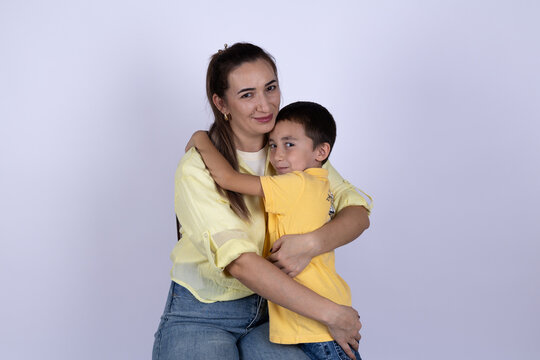 A woman is hugging a young boy in front of a plain background