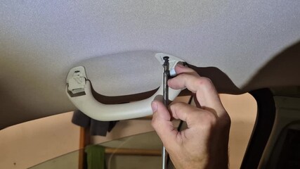 Car grab handle unscrewing, person's hand removing an interior ceiling handle from a vehicle for maintenance or repair