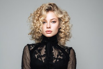 Attractive young woman in a black dress with curly blonde hair in a retro style photographed in a studio
