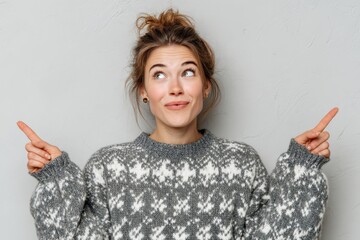 A young attractive woman in a winter sweater at home looks up in astonishment pointing with raised arms
