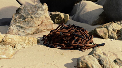 A cluster of rusted chains lies on the sandy surface, surrounded by various rocks.