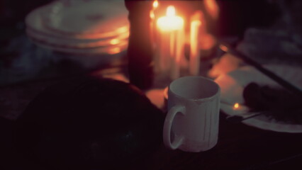 Soft candlelight flickers as an empty cup sits beside stacked plates, creating a warm and inviting atmosphere for a gathering. The scene feels intimate and peaceful.