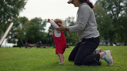 Mother helping toddler take first steps in park, child learning to walk but starting to crawl instead, showing tenderness, encouragement, and early milestones of growth and connection