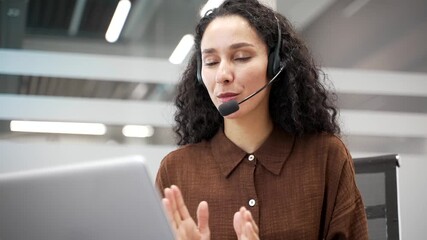 Smiling businesswoman in a wireless headset talking on a video call using a laptop sitting in office. Female manager communicates at an online conference or chats remotely with a business partner. Clo - Powered by Adobe