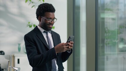 African American businessman smiling looking at smartphone in modern office happy male professional business man reading message using mobile phone digital communication success corporate workplace - Powered by Adobe