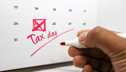 A hand marking Tax day and crossing out the 25th on a calendar with a red marker.