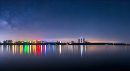Obraz premium Stunning city skyline reflected in calm waters under a starry night sky creates a peaceful and vibrant urban landscape for travel and lifestyle brands
