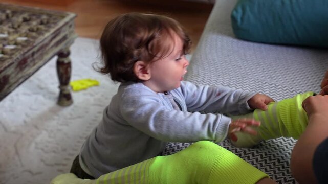 Smiling toddler leaning on sibling&rsquo;s legs while playing in cozy living room, expressing joy, curiosity, and warmth in a familiar family environment