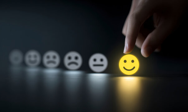 Hand selects a bright, yellow smiley face from a row of gray emoticons.