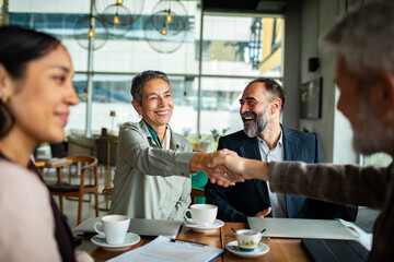 Mature business colleagues smiling during handshake in cafe