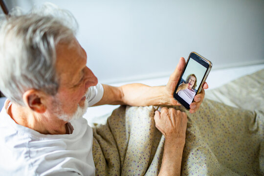 Senior man smiling while video calling wife at home in bed