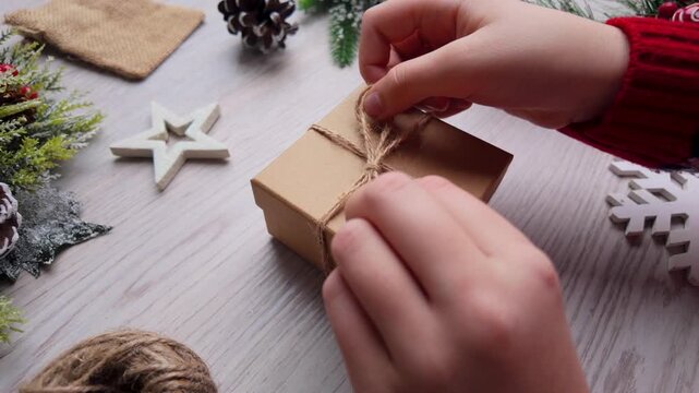 Normal-speed close-up of hands tying natural twine around an eco-friendly holiday gift wrapped in kraft paper
