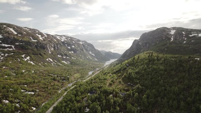 Aerial view of a lush green valley, nestled between rocky mountains with snow patches, under a soft, diffused sunlight, Dalen, Telemark, Norway.