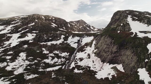 Aerial view of snow-dusted mountains and a cascading waterfall creates a striking contrast against the rugged terrain, Dalen, Telemark, Norway.