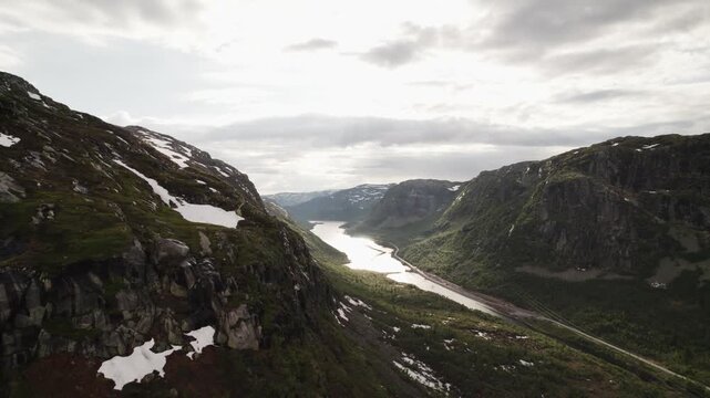 Aerial view of rugged mountainsides descending to meet the reflective waters of a river under a cloudy sky, Dalen, Telemark, Norway.