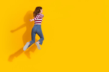 Young girl jumps in mid air against bright yellow background wearing striped top and jeans for lively fashion lifestyle and advertising use