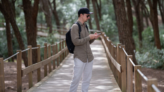 Traveler on forest boardwalk looking at smartphone, hiking Portugal