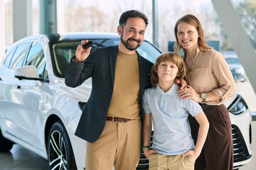 Caucasian middle aged man holding car key standing with Caucasian middle aged woman and Caucasian boy