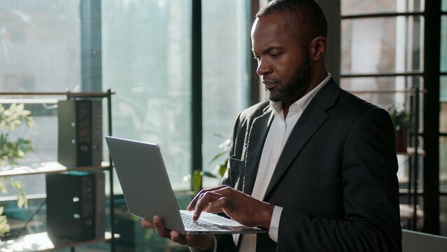 African American ethnic business man concentrated businessman typing laptop online software chatting in office middle-aged male entrepreneur in sunlight office indoors using computer programming job