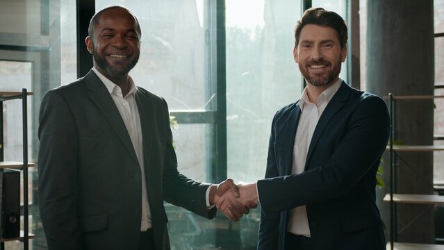 Two diverse positive multiracial businessmen business team men handshaking meeting satisfied hiring job welcome office formal agreement colleagues handshake Caucasian African American managers work