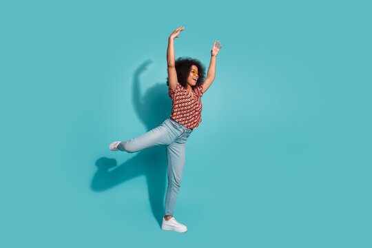 Young woman jumping with joyful expression in blue studio background wearing casual print shirt and jeans for lifestyle fashion stock photo