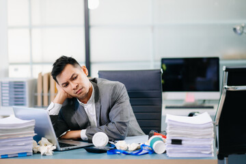 Exhausted businessman holding coffee cup at desk, feeling tired and overworked with paperwork and deadlines in modern office environment.