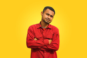 A black young man stands with folded arms against a yellow background, expressing a mix of confidence and curiosity. Studio portrait with bold colors, suitable for advertising and lifestyle themes.