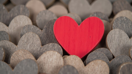Vibrant red heart stands out among collection of muted wooden hearts, symbolizing love and affection in charming display