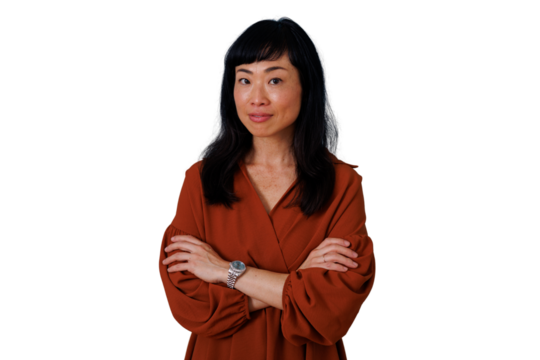 Confident asian woman with bangs standing, arms crossed, wearing a solid rust-colored blouse on transparent background - Powered by Adobe